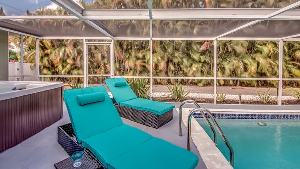 A poolside area with two lounge chairs, a hot tub, and a view of palm trees. - Pool - Hot Tub - BBQ - Private Backyard (Cape Coral)