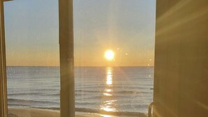 Une vue sur l’océan, avec le soleil se couchant ou se levant, visible à travers une porte vitrée.