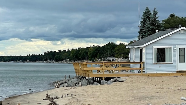 Une maison de plage avec une terrasse en bois, un petit abri de jardin et une vue sur l’eau.