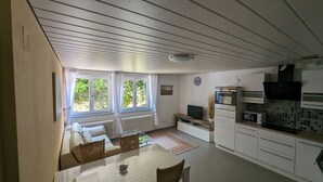 Et kompakt køkken med spiseplads, en radiator, et fjernsyn og et ur på væggen.