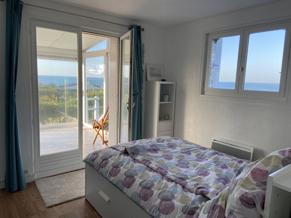 Un dormitorio con cama, escritorio, silla y vista al mar a través de una puerta corrediza.
