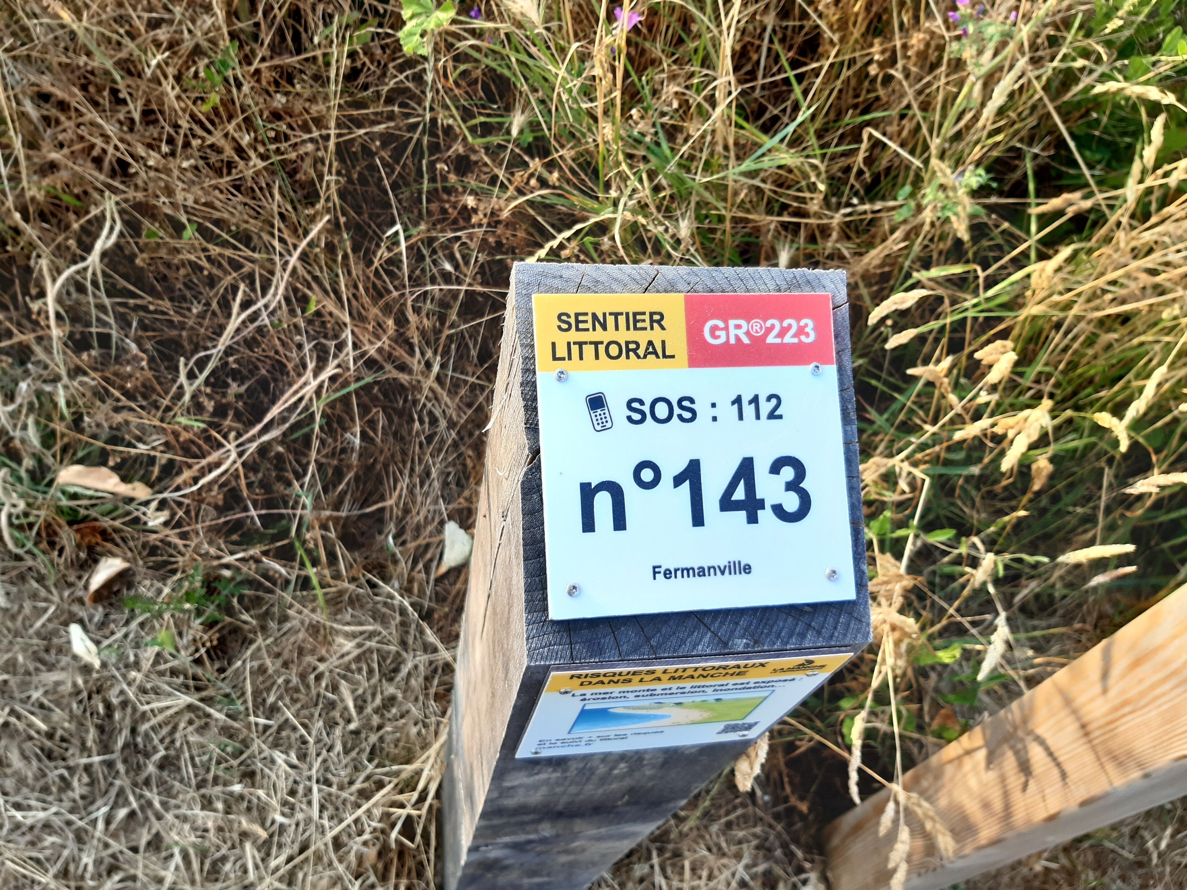 A sign with text and symbols, including "SENTIER LITTORAL GR 223," "SOS: 112," and "n°143."
