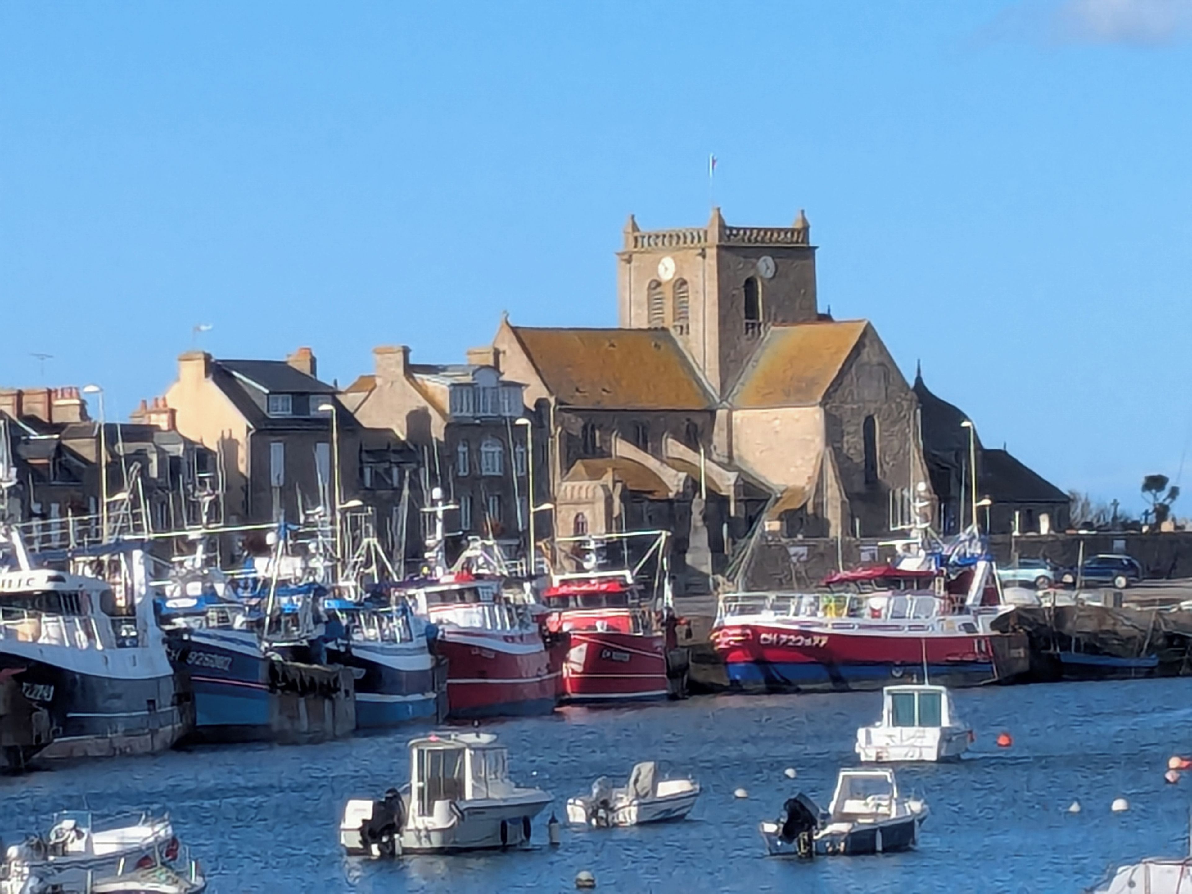 Un puerto con barcos amarrados, una iglesia con campanario y edificios residenciales.