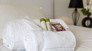 Un lit bien fait, avec une serviette blanche, deux bouteilles de shampoing et un savon.