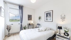 Une chambre à coucher comprenant un lit, des tables de chevet, une fenêtre avec des rideaux, un radiateur et des œuvres d’art murales.