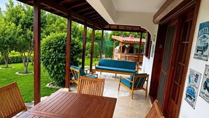 Eine Terrasse im Freien mit Holztisch und -stühlen, einem Grill und Blick auf einen Garten.