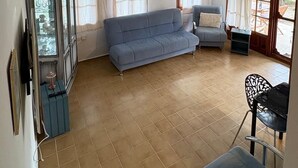 Ein geräumiges Wohnzimmer mit einem blauen Sofa, einem kleinen Tisch und einem Fernseher auf einem Schrank.