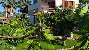 Ein zweistöckiges Haus mit rotem Ziegeldach, einem Balkon und einem Garten mit großen, grünen Blättern.