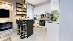 Una cocina moderna con armarios blancos, horno empotrado, microondas y estufa a gas. Hay una barra con taburetes y una botella de vino.