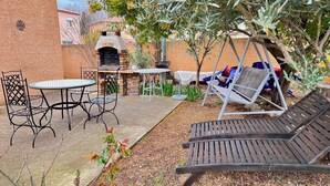 Une terrasse extérieure avec un four en briques, des chaises en métal, une table et une chaise suspendue.