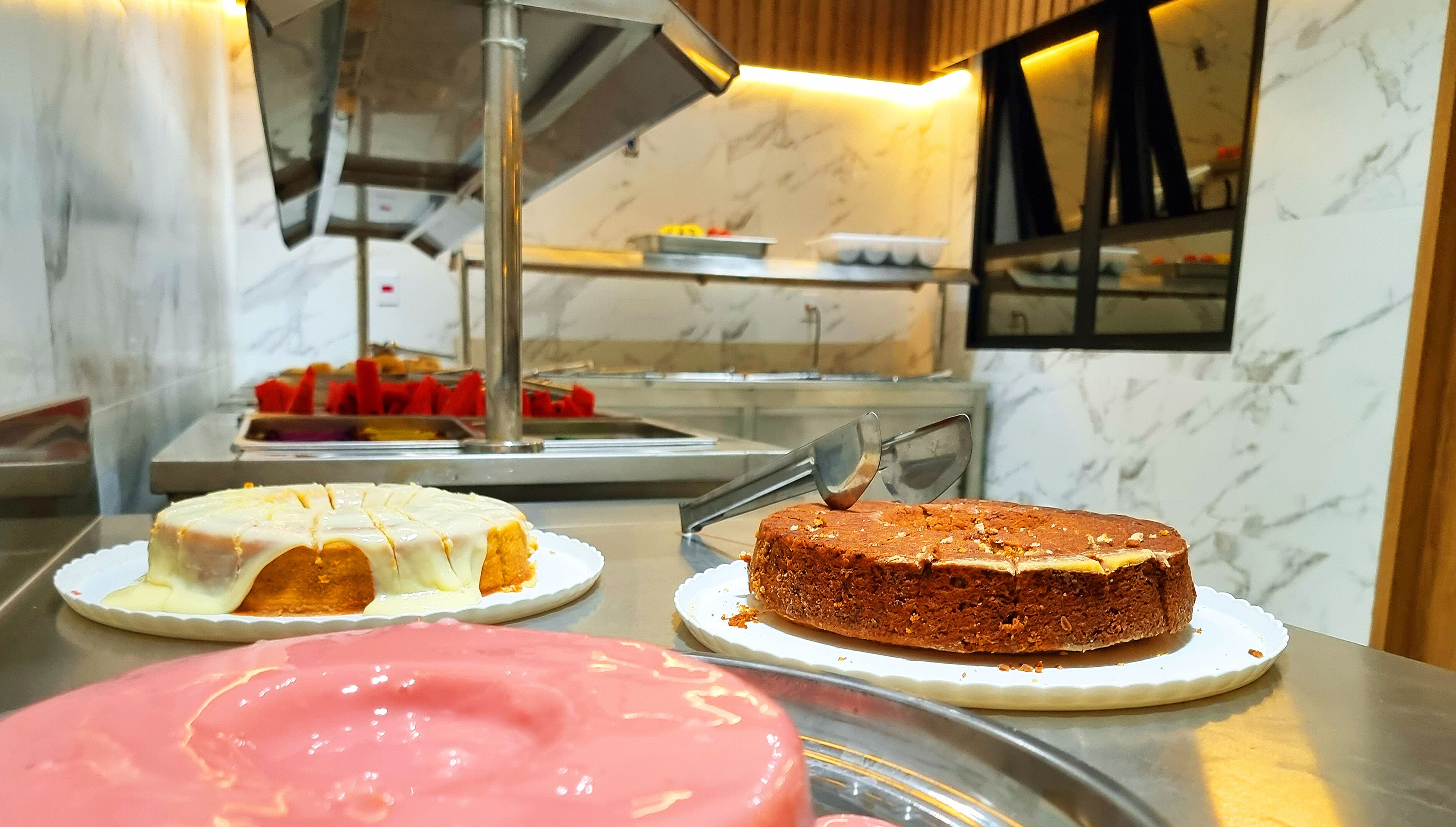 A dessert display with cakes and a pink dessert on a counter.