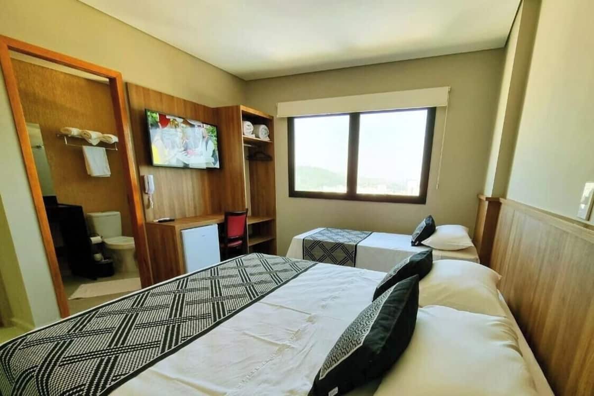 Une chambre d’hôtel avec deux lits, une télévision, une fenêtre et une armoire en bois.