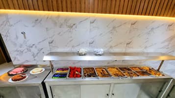 A buffet setup with various food items and a marble wall background.