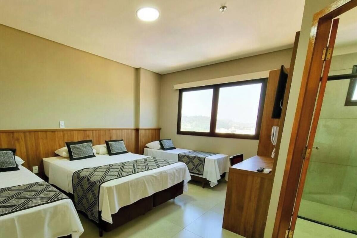Une chambre d’hôtel avec trois lits, une tête de lit en bois, une fenêtre et un comptoir de réception.