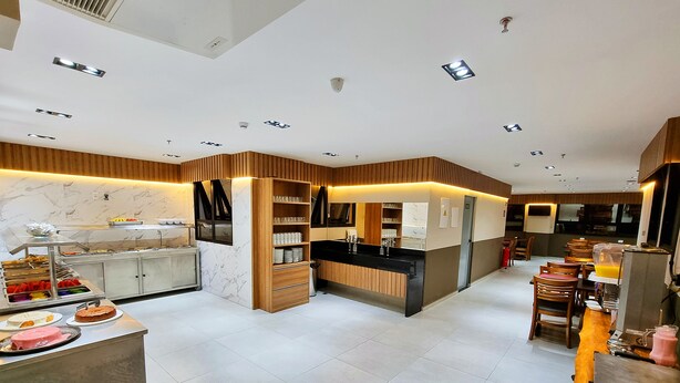 A modern hotel lobby with a marble reception desk, a buffet area with various food items, and a seating area with wooden chairs and tables. - VIPPER Hotel (Aparecida)