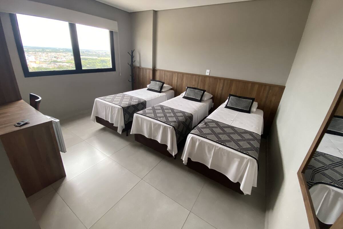 Une chambre d’hôtel avec trois lits, un bureau en bois et une fenêtre donnant sur la ville.