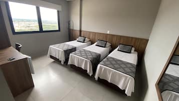 Hotellihuone, jossa on kolme sänkyä, puinen työpöytä ja ikkuna, josta avautuu näkymä kaupunkiin.