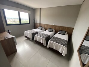 A hotel room with three beds, a wooden desk, and a window with a city view.