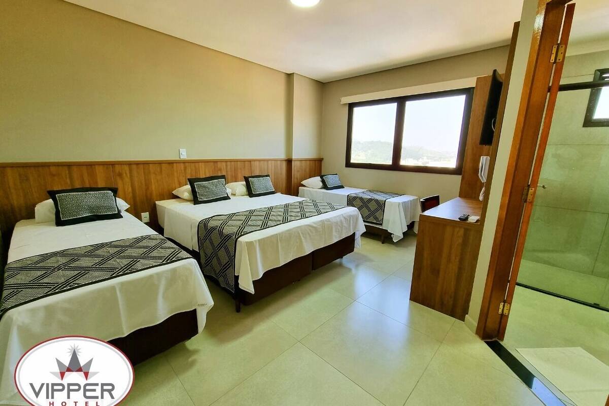 Une chambre d’hôtel avec trois lits, une tête de lit en bois, une fenêtre et un espace douche.
