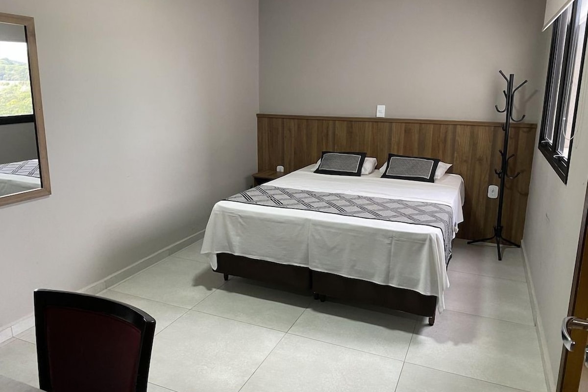 A hotel room with a bed, a chair, a coat rack, and a window.