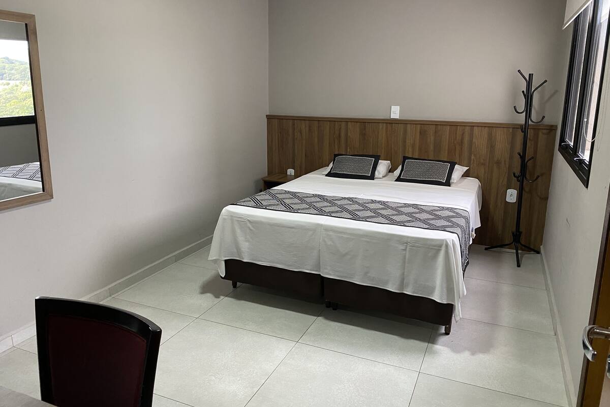 Une chambre à coucher avec un lit, une chaise, un porte-manteau et une fenêtre.