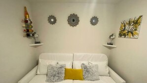 A white sofa with two grey and one yellow pillow, a decorative bottle holder, and three wall-mounted flower-like decorations. - Yellow Royal Family Suit 2brs, 3beds, 2bths, Pool (Portmore)