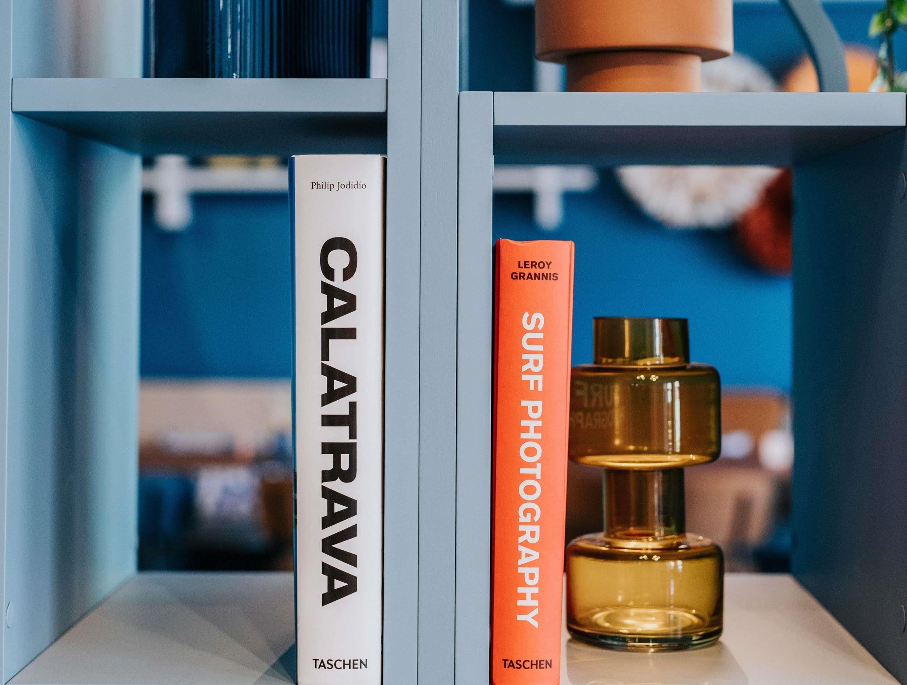Two books titled 'CALATRAVA' and 'SURF PHOTOGRAPHY' by LEROY GRANNIS, placed on a shelf with a bottle of perfume.
