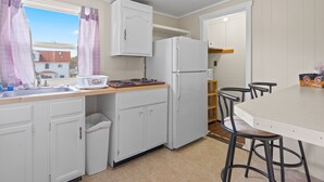 A compact kitchen with white cabinets, a refrigerator, a sink, and a dining area with stools. - Beach Motel & Suites (Old Orchard Beach)