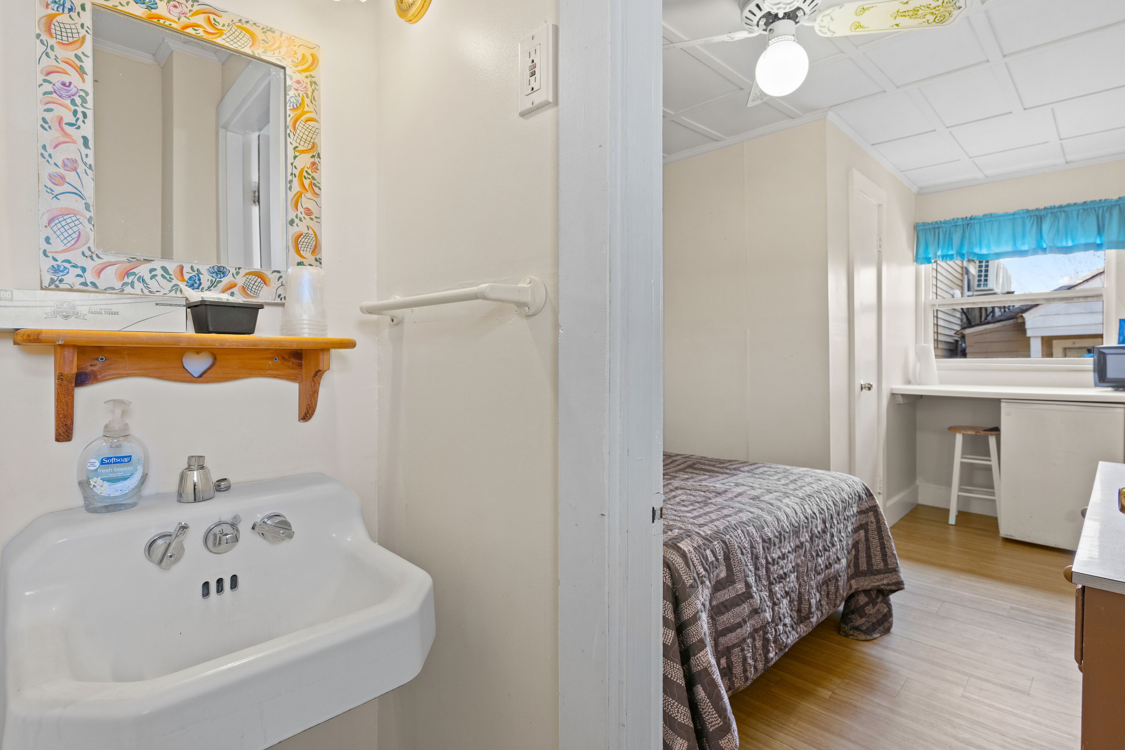 A bathroom with a white sink, a mirror with a colorful frame, and a shower area.