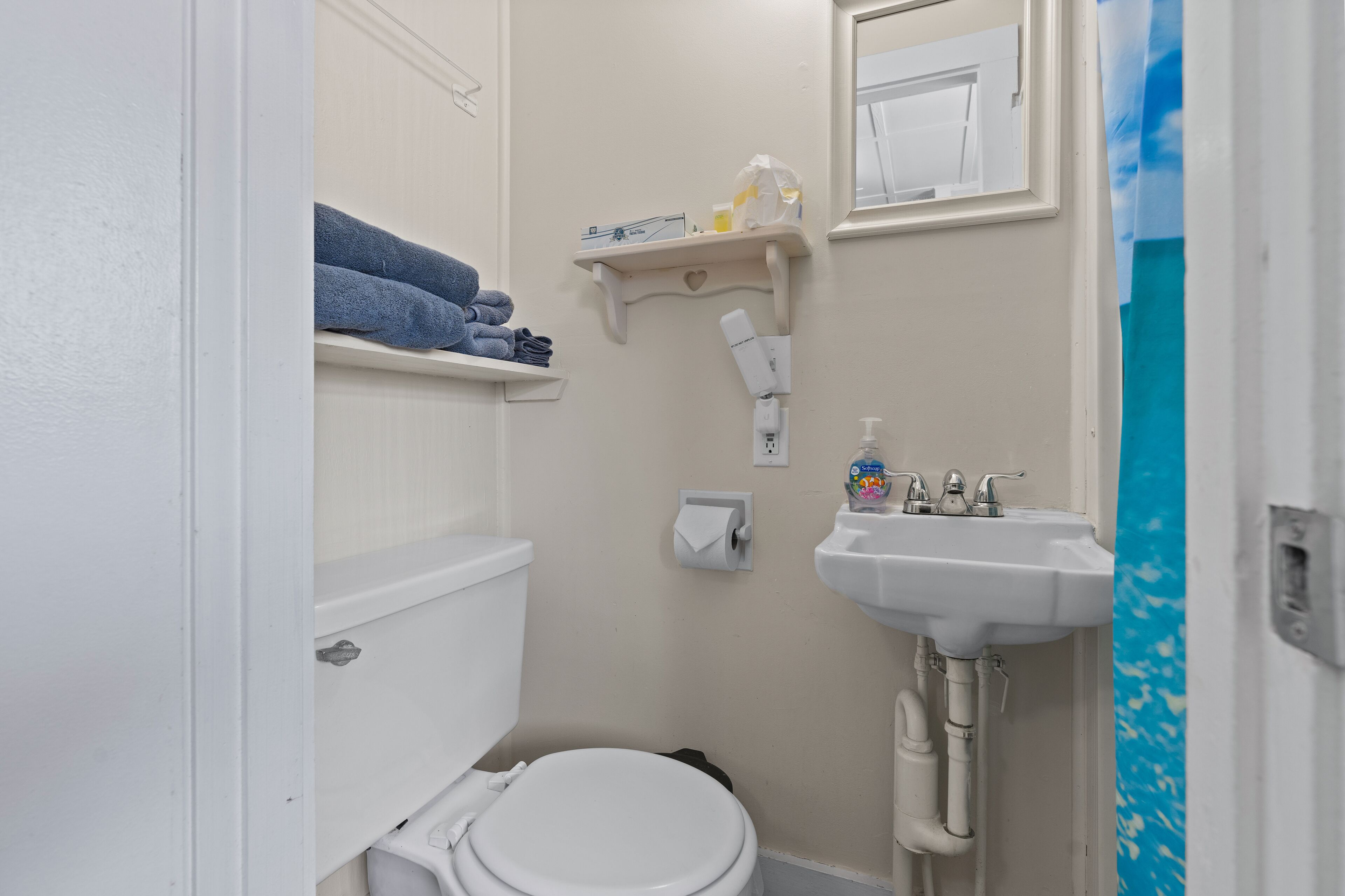 A bathroom with a toilet, a sink, and a shelf with towels.
