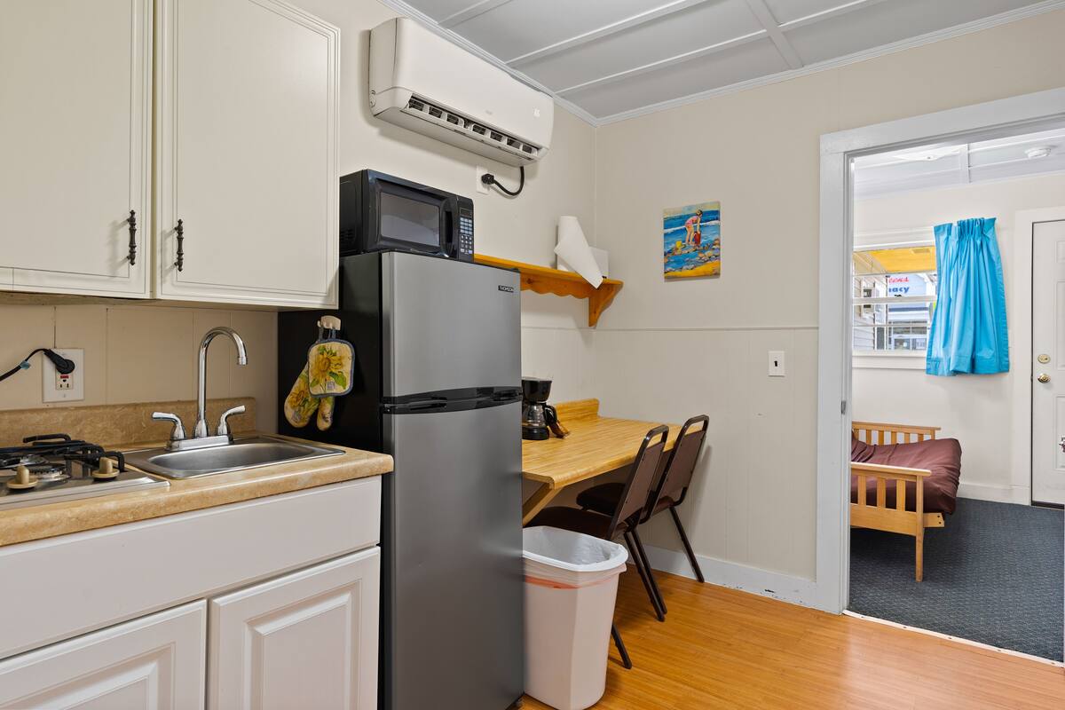 A compact kitchen with a refrigerator, microwave, sink, and a small dining area with a chair and table.
