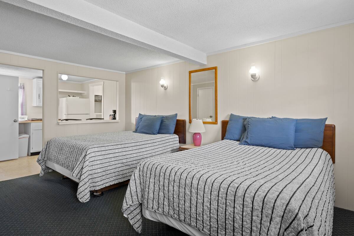 A hotel room with two beds, a mirror, a nightstand, and a lamp.