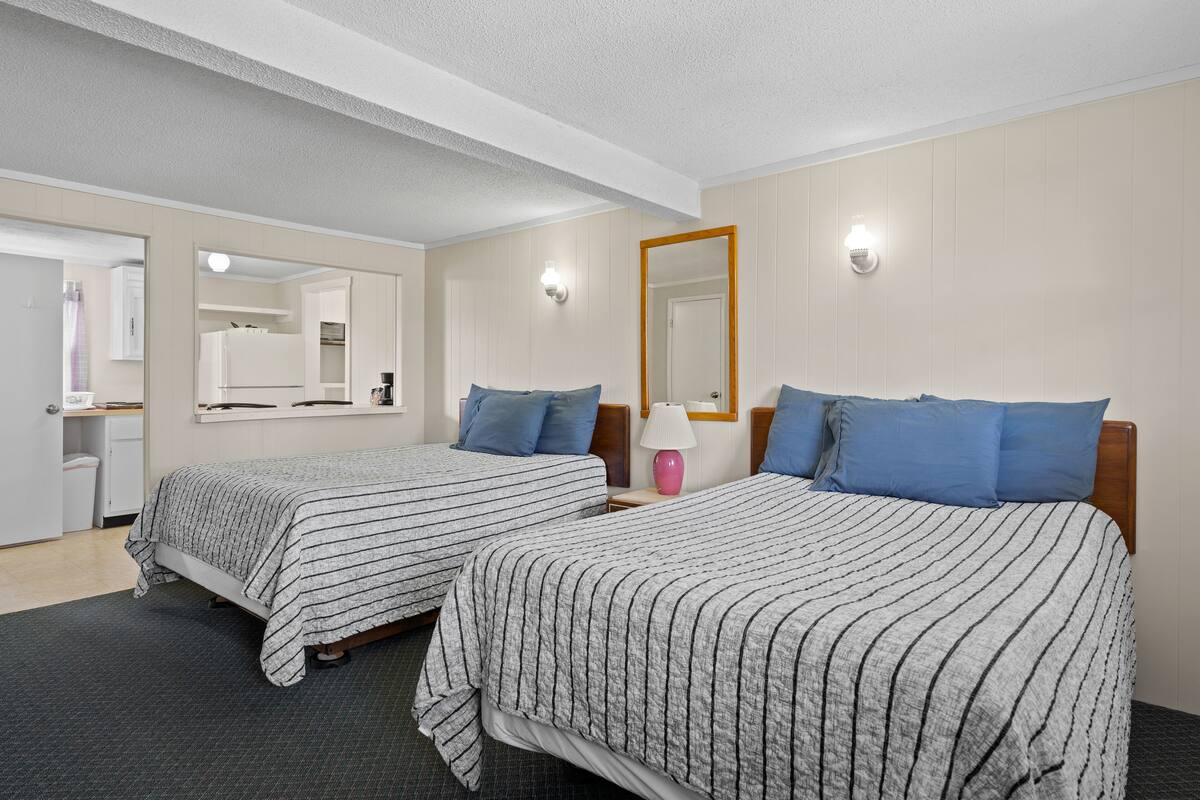 A hotel room with two beds, a mirror, a lamp, and a small table.