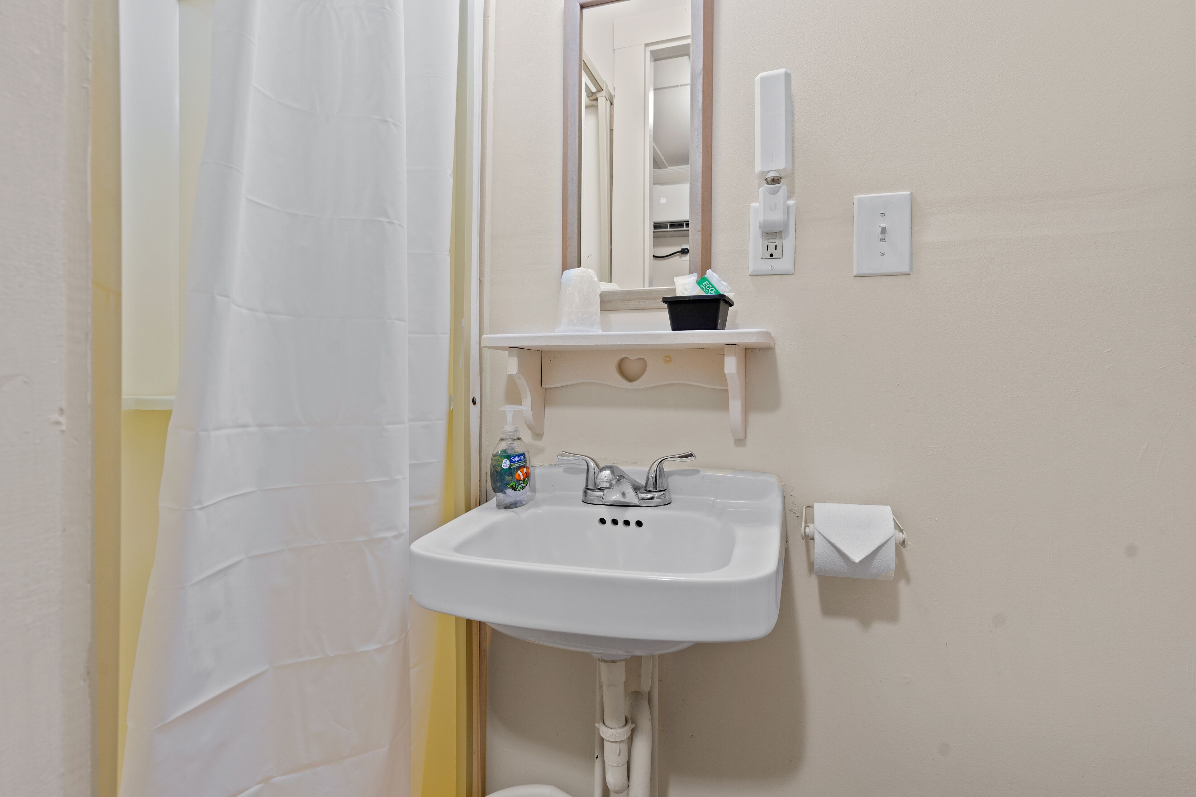 A bathroom with a white sink, a mirror, a soap dispenser, and a toilet paper holder.