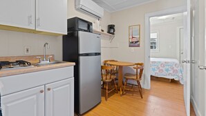 A compact kitchen with a refrigerator, microwave, and stove. There is a dining area with a table and chairs. A bed is visible in the adjacent room. - Beach Motel & Suites (Old Orchard Beach)
