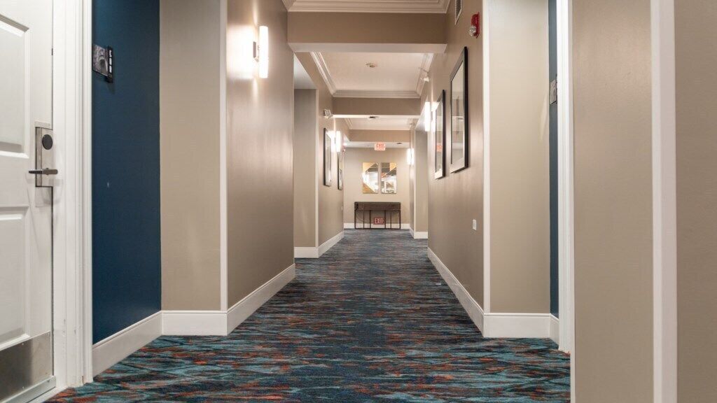 A hotel hallway with a patterned carpet, beige walls, and framed pictures on the walls.