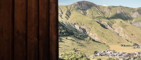 Vista a través de una ventana de madera de un valle con colinas verdes y un pequeño pueblo.