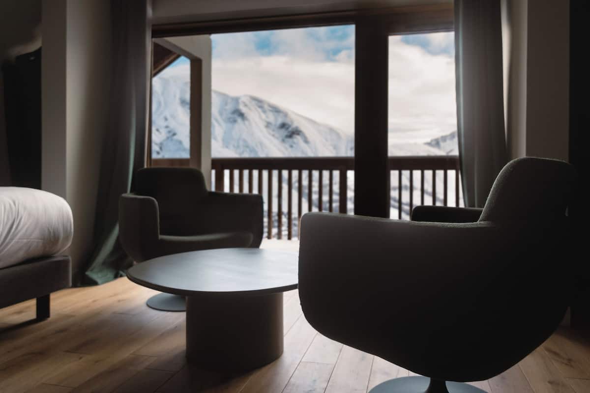 Una habitación de hotel moderna con un ventanal grande, una mesa redonda, dos sillas y una cama.
