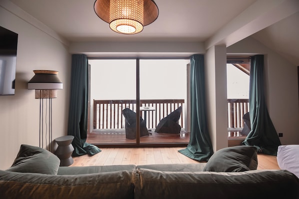 Ein modernes Wohnzimmer mit einer Couch, einer Stehlampe und Blick auf einen Balkon mit Gartenmöbeln.