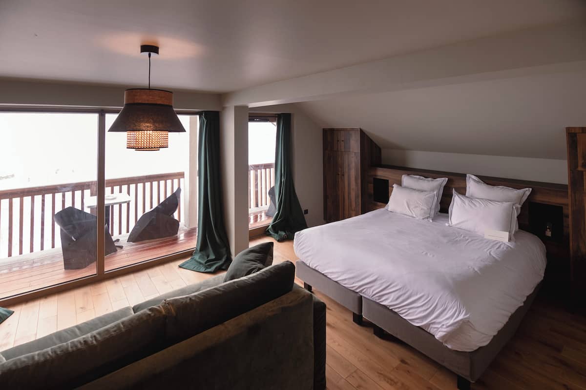 Un dormitorio con una cama grande, un sofá, una lámpara colgante y vistas a través de una ventana.