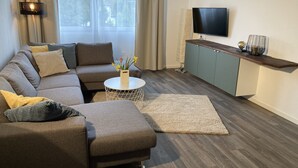 A modern living room with a sectional sofa, a round coffee table, and a flat-screen TV mounted on the wall. - Vacation cottage by the lake (Möhnesee)