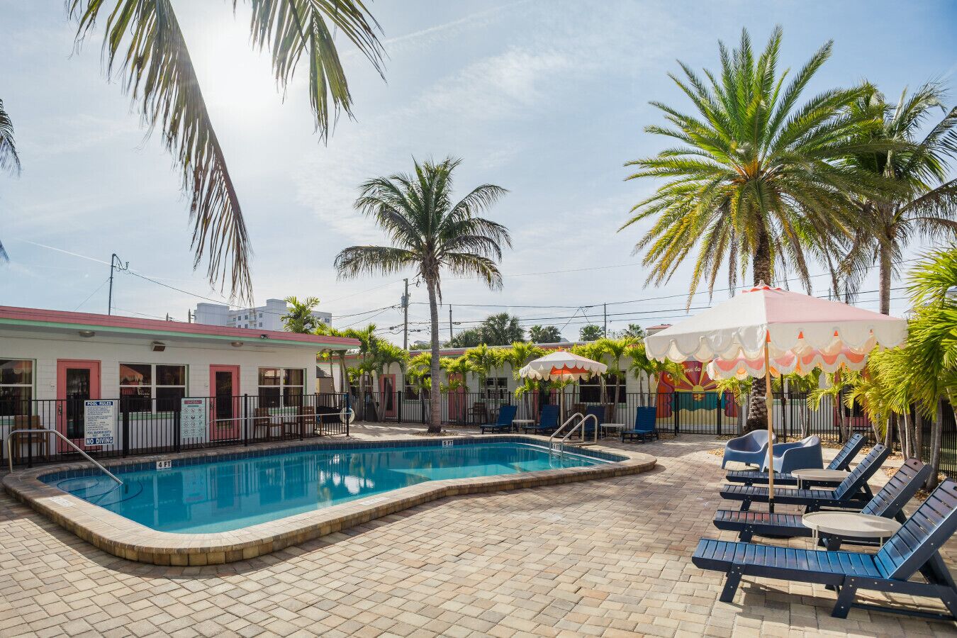 A swimming pool with lounge chairs, palm trees, and a building with a red roof.
