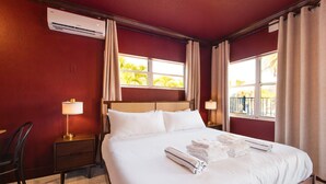 Habitación de hotel con una cama grande, una mesita de noche, una lámpara, un equipo de aire acondicionado y una ventana con cortinas.