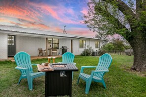 A house with a patio area featuring a grill and two turquoise chairs.