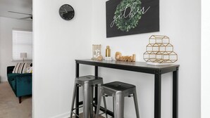 A modern living room with a black metal console table, two metal stools, a wall clock, and a decorative piece with the word "gather" on the wall.