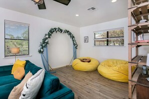 A room with a teal sofa, yellow bean bag chairs, a wooden bookshelf, and a decorative arch.