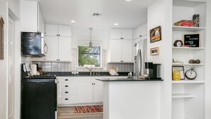 A modern kitchen with white cabinetry, a black stove, and a coffee station.
