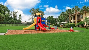 A playground with slides and climbing structures, surrounded by a well-maintained lawn and a building in the background.