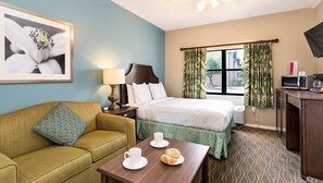 A hotel room with a bed, a sofa, a table with breakfast items, a TV, and a window with curtains.