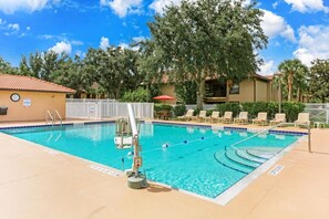 A swimming pool with a lifeguard stand, lounge chairs, and a fenced area.